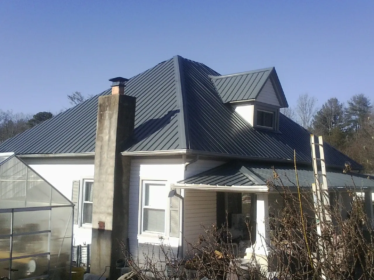 Dark blue standing seam metal roof on a white farmhouse with dormer — Slate & Tile Roof Repair by Roofing Brothers in Proctorsville