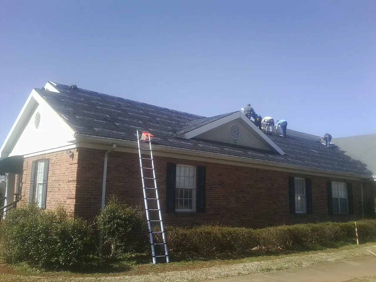 Crew tearing shingles off a brick ranch roof with a ladder set — Emergency Roof Repair work by our crew in Proctorsville