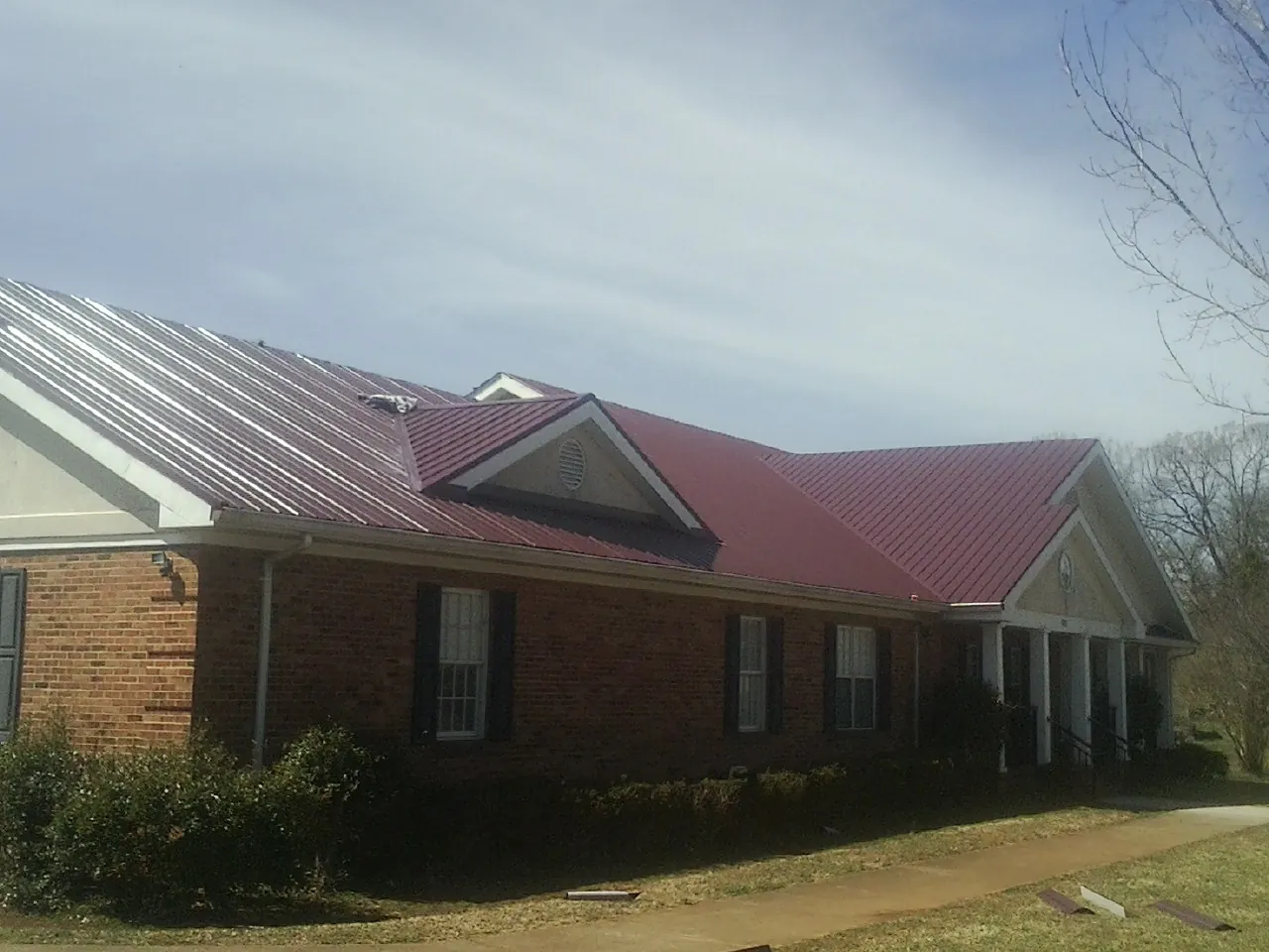 Red metal roof with gabled entries on a long brick building, from a Hail Damage Roof Repair job in Proctorsville