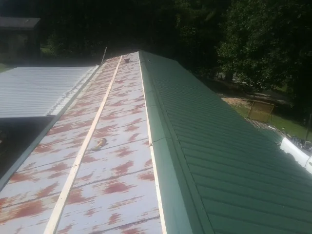 Old rusted panels beside newly installed green metal roofing — Wind Damage Roof Repair by Roofing Brothers in Proctorsville