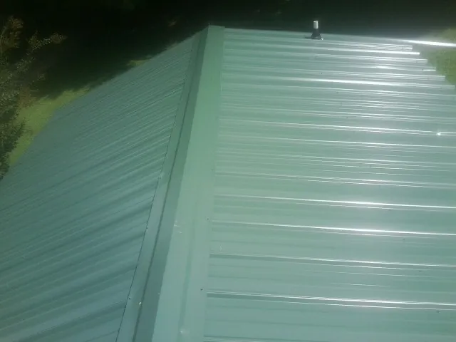 New green metal panels meeting at the ridge of a roof — Flat Roof Repair work by our crew in Proctorsville