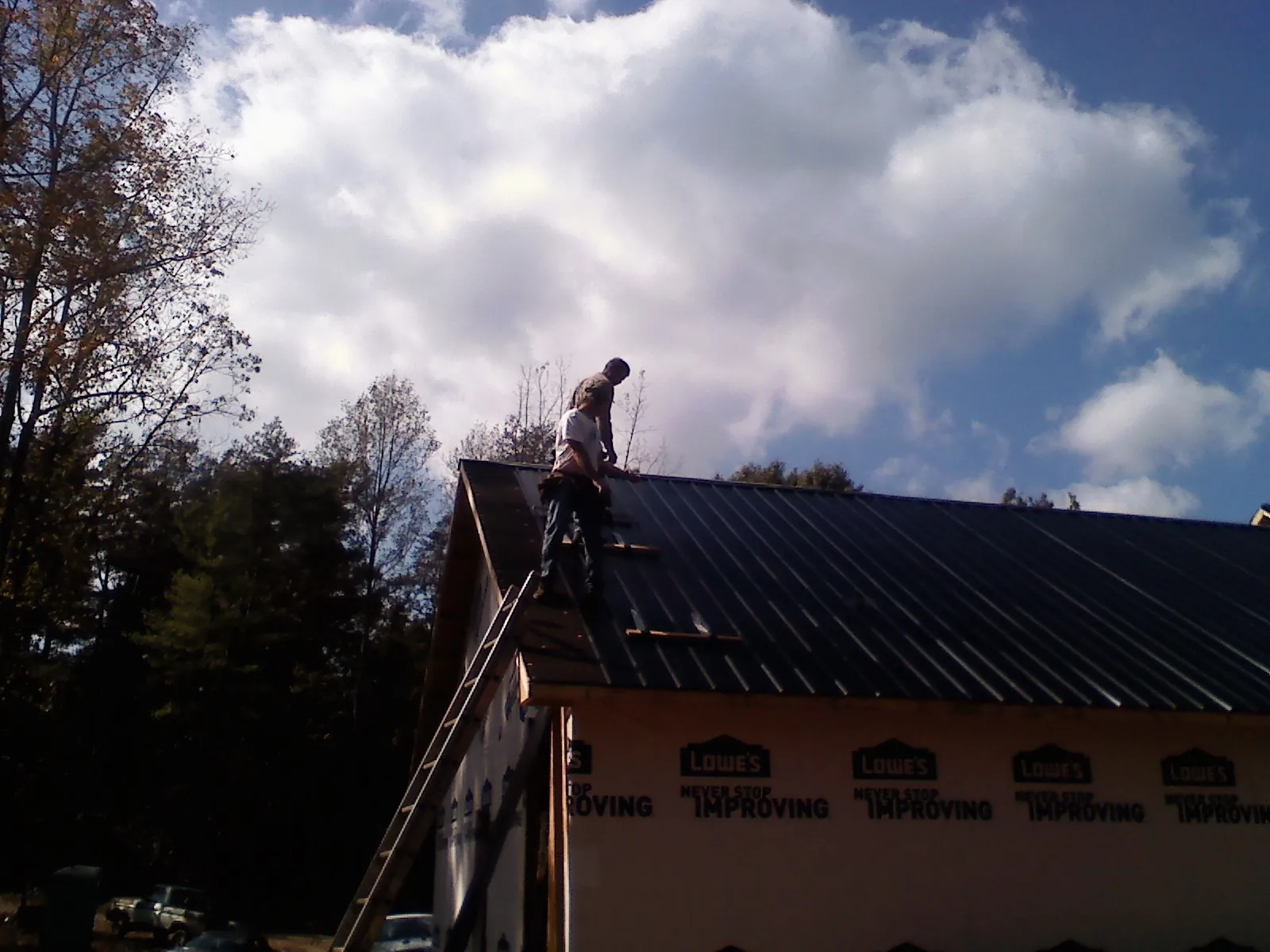 Roofer fastening dark metal panels high against a cloudy sky, from a Roof Inspection job in Proctorsville