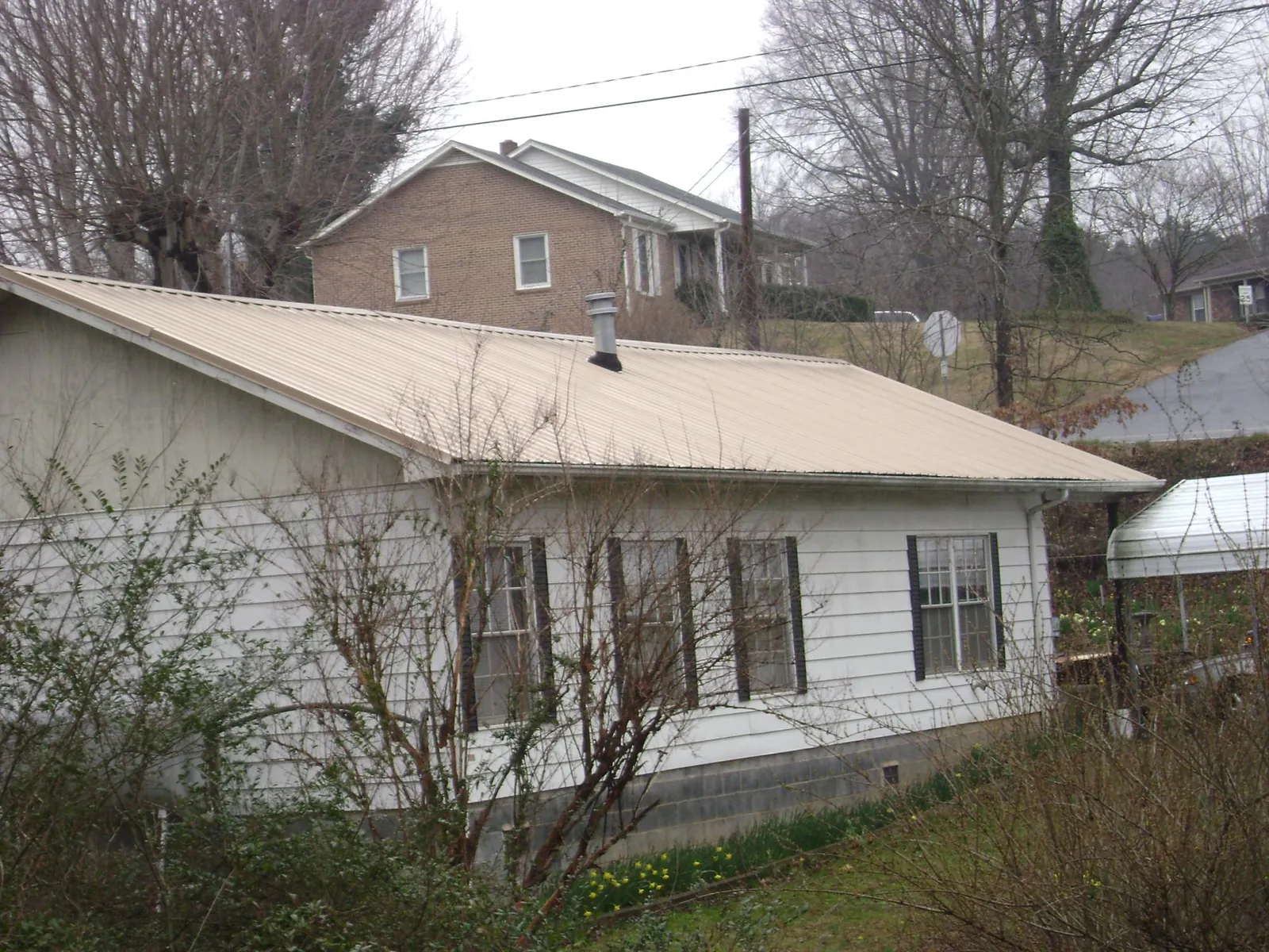 Tan metal roof on a white sided house set into a hillside — Commercial Roofing by Roofing Brothers in Proctorsville